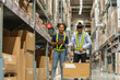 © supAVADEE BUTRADEE - frican American female employee in a warehouse with an Asian male employee  walking and talking together in wholesale shop.Teamwork concept.