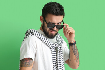 Poster - Fashionable bearded man wearing sunglasses and winking on green background