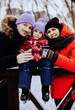 Happy mother, father and daughter drinking hot tea at outdoor skating rink in winter