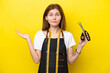 Young seamstress English woman isolated on yellow background having doubts while raising hands