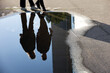 View to puddle on a street with reflection of walking couple. Rain in summer city, wet asphalt