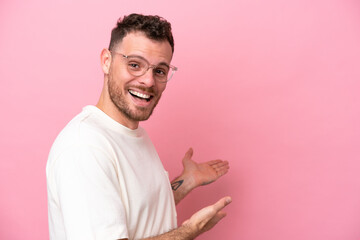 Wall Mural - Young brazilian man isolated on pink background With glasses and presenting something