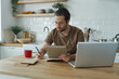 © gstockstudio - Handsome young man using technologies while working at the kitchen island at home
