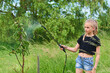 Teenage girl spraying ecological product against aphids and other pests on fruit trees and other trees in the garden and orchard. Selective focus