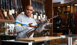 © JackF - Confident latin american man owner of armory shop standing behind counter and offering vintage hunting carbine rifle with wooden butt