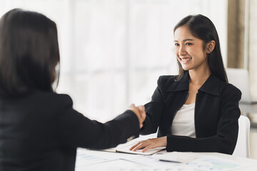 Aufkleber - Two Businesswomen Shaking Hands In Modern Office, Smiling young businesswoman shaking hands with a coworker during a meeting with colleagues around a table in an office boardroom.