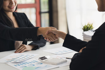 Aufkleber - Two Businesswomen Shaking Hands In Modern Office, Smiling young businesswoman shaking hands with a coworker during a meeting with colleagues around a table in an office boardroom.