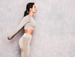 © halayalex - Fitness confident woman in sports clothing. Sexy young beautiful model with perfect body. Female posing near grey urban wall in studio. Stretching out before training