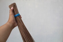 Left Hand Holding A Broom Stick Against A White Wall Background. House Cleaning Concept