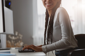 Wall Mural - close up shot of young smiled female sitting at desk in apartment working on computer