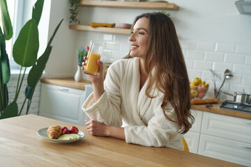 Sticker - Happy young woman in bathrobe having breakfast at the modern kitchen