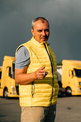 Wall Mural - Mature middle age man standing at trucks parking and talking on sunny day. Manager of warehouse or driver