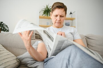 Canvas Print - middle aged woman sitting sofa and reading newspapers.