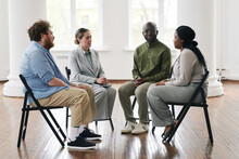 Group Of Interracial People Listening To Young African American Female Patient Of Psychotherapist While Sitting On Chairs In Circle