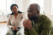 © pressmaster - Sad African American man sitting in front of camera with his hands clasped while counselor comforting him during psychological session