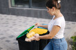 © Aleksandr - Sede view of female hold two cardboard tray of eggs. Rubbish, egg carton and thowing into recycling bins. Close-up of woman stand by blue, yeallow and open green bin