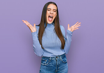 Wall Mural - Young beautiful woman wearing casual winter sweater celebrating mad and crazy for success with arms raised and closed eyes screaming excited. winner concept