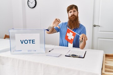 Poster - Caucasian man with long beard at political campaign election holding swiss flag with angry face, negative sign showing dislike with thumbs down, rejection concept