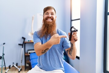 Poster - Young redhead man wearing physiotherapist uniform holding hand grip at physiotherapy clinic