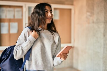 Wall Mural - Young middle east student girl smiling happy using smartphone at the city.