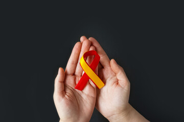 World hepatitis day. Adult hands holding red yellow ribbon on black background. Awareness of prevention and treatment viral hepatitis. Liver cancer. World cancer day. copy space. banner