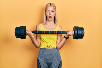 Poster - Beautiful blonde woman wearing sportswear using dumbbells afraid and shocked with surprise and amazed expression, fear and excited face.