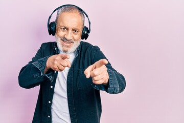 Canvas Print - Handsome senior man with beard listening to music using headphones pointing fingers to camera with happy and funny face. good energy and vibes.