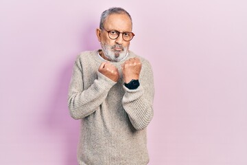 Canvas Print - Handsome senior man with beard wearing casual sweater and glasses ready to fight with fist defense gesture, angry and upset face, afraid of problem