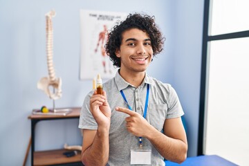 Sticker - Hispanic man with curly hair holding cbd oil smiling happy pointing with hand and finger to the side