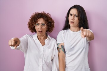 Sticker - Hispanic mother and daughter wearing casual white t shirt over pink background pointing displeased and frustrated to the camera, angry and furious with you