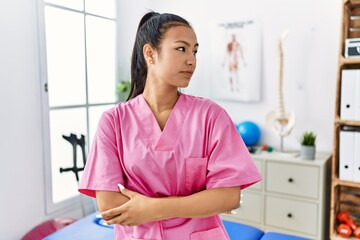 Sticker - Young hispanic woman working at pain recovery clinic looking to side, relax profile pose with natural face with confident smile.