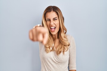 Wall Mural - Young blonde woman standing over isolated background pointing displeased and frustrated to the camera, angry and furious with you