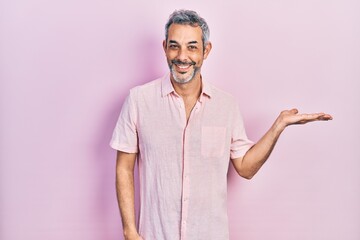 Canvas Print - Handsome middle age man with grey hair wearing casual shirt smiling cheerful presenting and pointing with palm of hand looking at the camera.