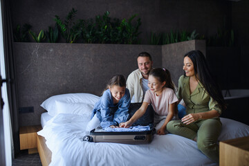 Wall Mural - Happy young family with two children sitting on bed and unpacking at luxury hotel, summer holiday.