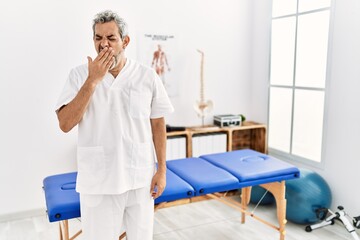 Sticker - Middle age hispanic therapist man working at pain recovery clinic bored yawning tired covering mouth with hand. restless and sleepiness.