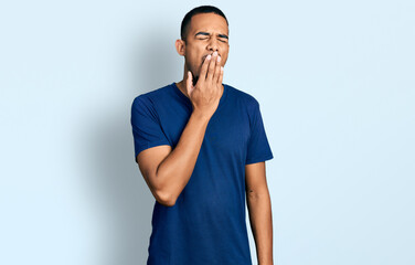 Young african american man wearing casual t shirt bored yawning tired covering mouth with hand. restless and sleepiness.