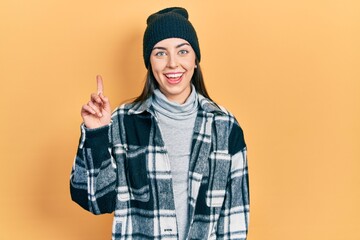 Poster - Beautiful woman with blue eyes wearing wool cap smiling with an idea or question pointing finger up with happy face, number one