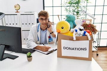 Sticker - Young caucasian man wearing doctor uniform talking on the smartphone at clinic