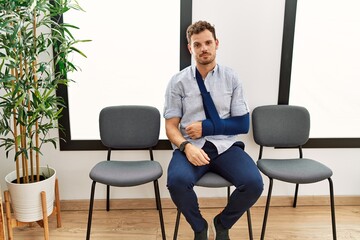 Poster - Handsome young man sitting at doctor waiting room with arm injury looking sleepy and tired, exhausted for fatigue and hangover, lazy eyes in the morning.