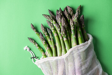 Asparagus. Fresh green asparagus in eco bag on greeen background. Vegan healthy food. Top view copy space