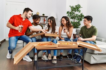 Wall Mural - Group of young friends smiling happy eating italian pizza sitting on the sofa at home.