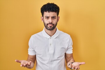 Sticker - Arab man standing over yellow background clueless and confused with open arms, no idea concept.