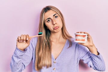 Poster - Beautiful hispanic woman holding denture and toothbrush depressed and worry for distress, crying angry and afraid. sad expression.