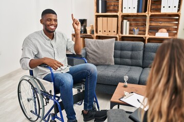 Sticker - African american man doing therapy sitting on wheelchair showing and pointing up with finger number one while smiling confident and happy.