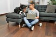 © Krakenimages.com - Young hispanic man using laptop sitting on the floor with dog at home.