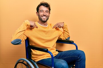 Canvas Print - Handsome man with beard sitting on wheelchair looking confident with smile on face, pointing oneself with fingers proud and happy.