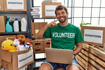 Sticker - Young handsome man wearing volunteer t shirt using laptop smiling cheerful showing and pointing with fingers teeth and mouth. dental health concept.