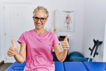 Sticker - Middle age blonde woman at pain recovery clinic success sign doing positive gesture with hand, thumbs up smiling and happy. cheerful expression and winner gesture.