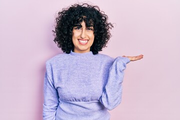 Sticker - Young middle east woman wearing casual clothes smiling cheerful presenting and pointing with palm of hand looking at the camera.