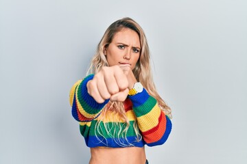 Sticker - Beautiful young blonde woman wearing colored sweater punching fist to fight, aggressive and angry attack, threat and violence